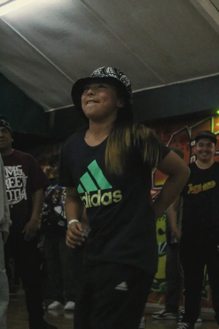 Una bailarina sonríe en la pista, con gorro y polera negra