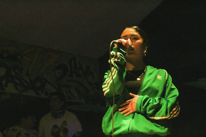 Una cantante con chaqueta verde, micrófono en mano