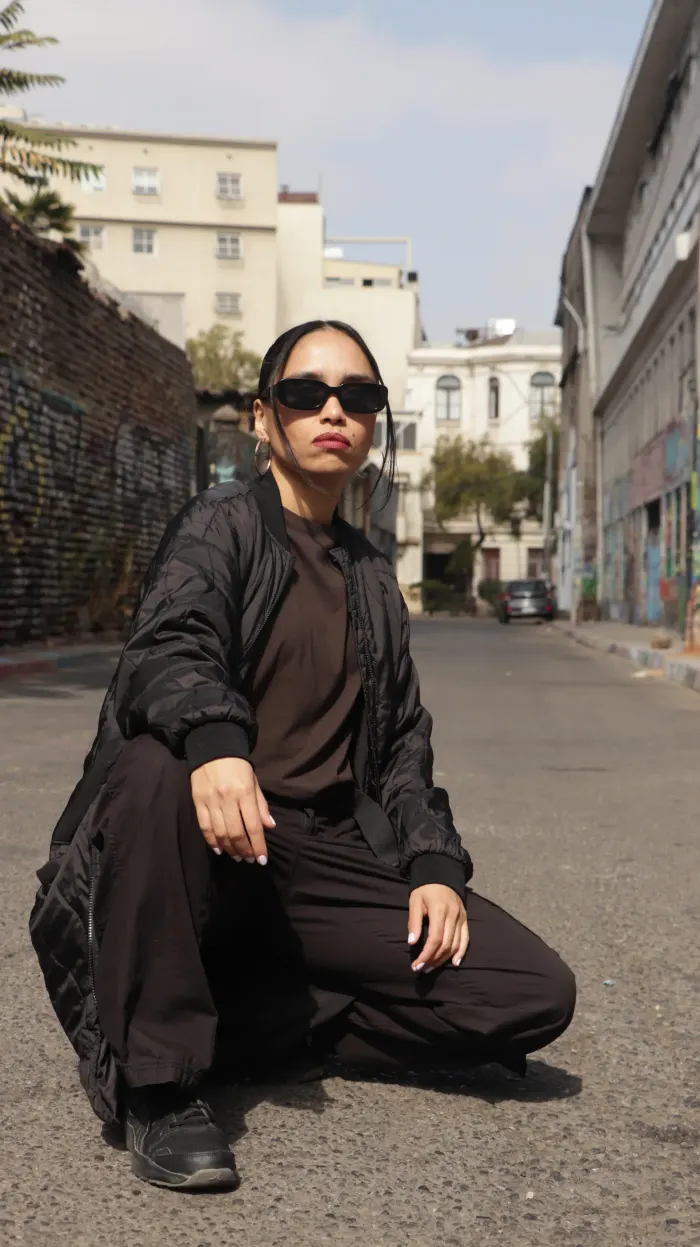 NayanCL agachada en la calle, con lentes oscuros