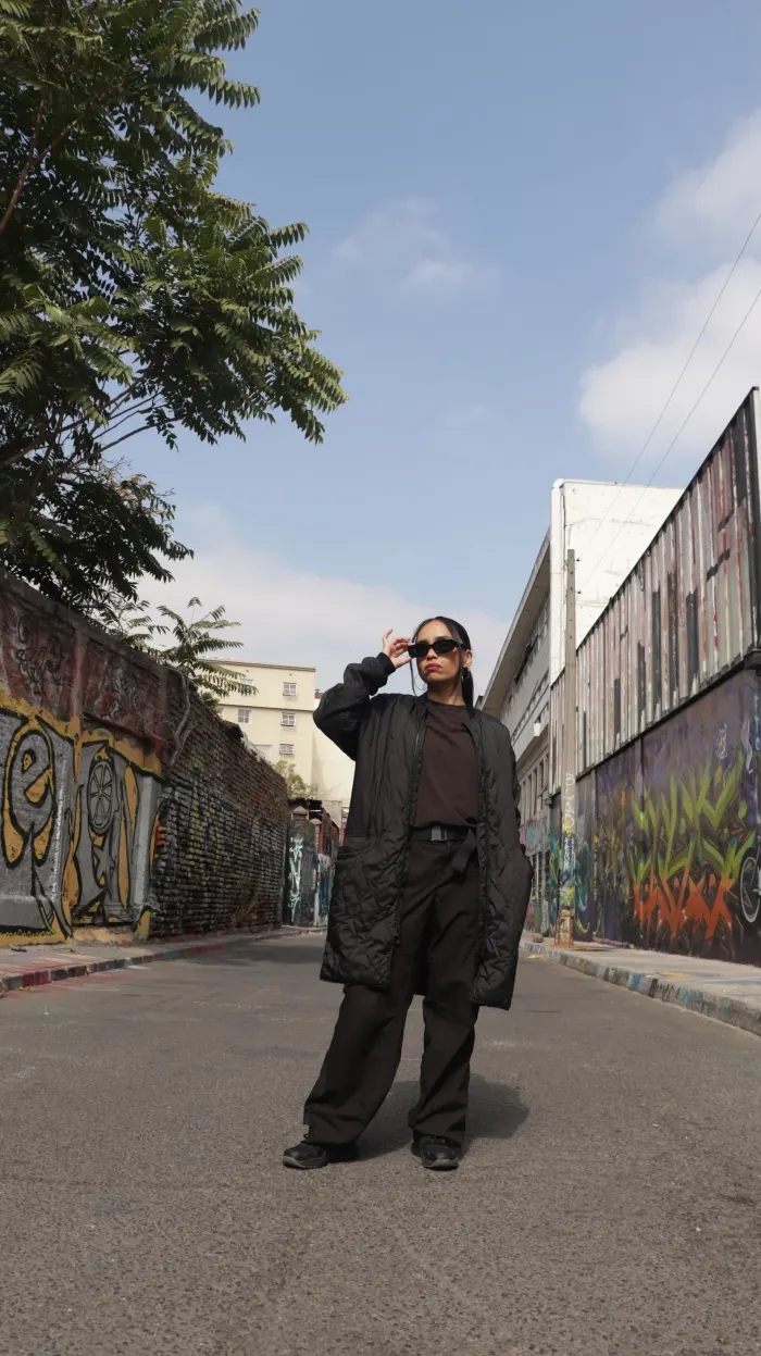 NayanCL de pie en una calle con graffiti, vestida de negro
